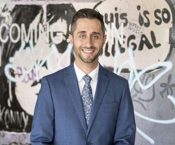 A man wearing a suit smiles for a photo in front of a graffiti wall